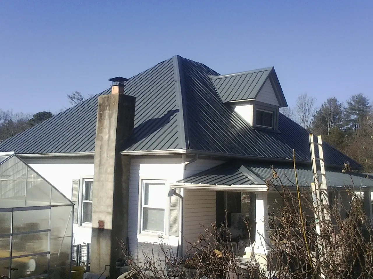 Dark blue standing seam metal roof on a white farmhouse with dormer — Slate & Tile Roof Repair by Roofing Brothers in Wellston