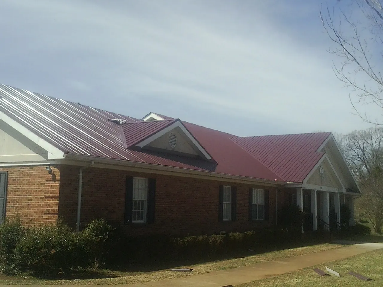 Red metal roof with gabled entries on a long brick building, from a Hail Damage Roof Repair job in Wellston