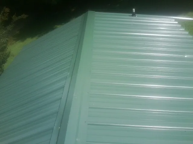 New green metal panels meeting at the ridge of a roof — Flat Roof Repair work by our crew in Wellston