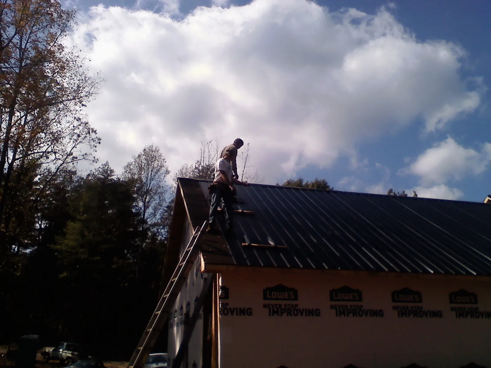 Roofer fastening dark metal panels high against a cloudy sky, from a Roof Inspection job in Wellston