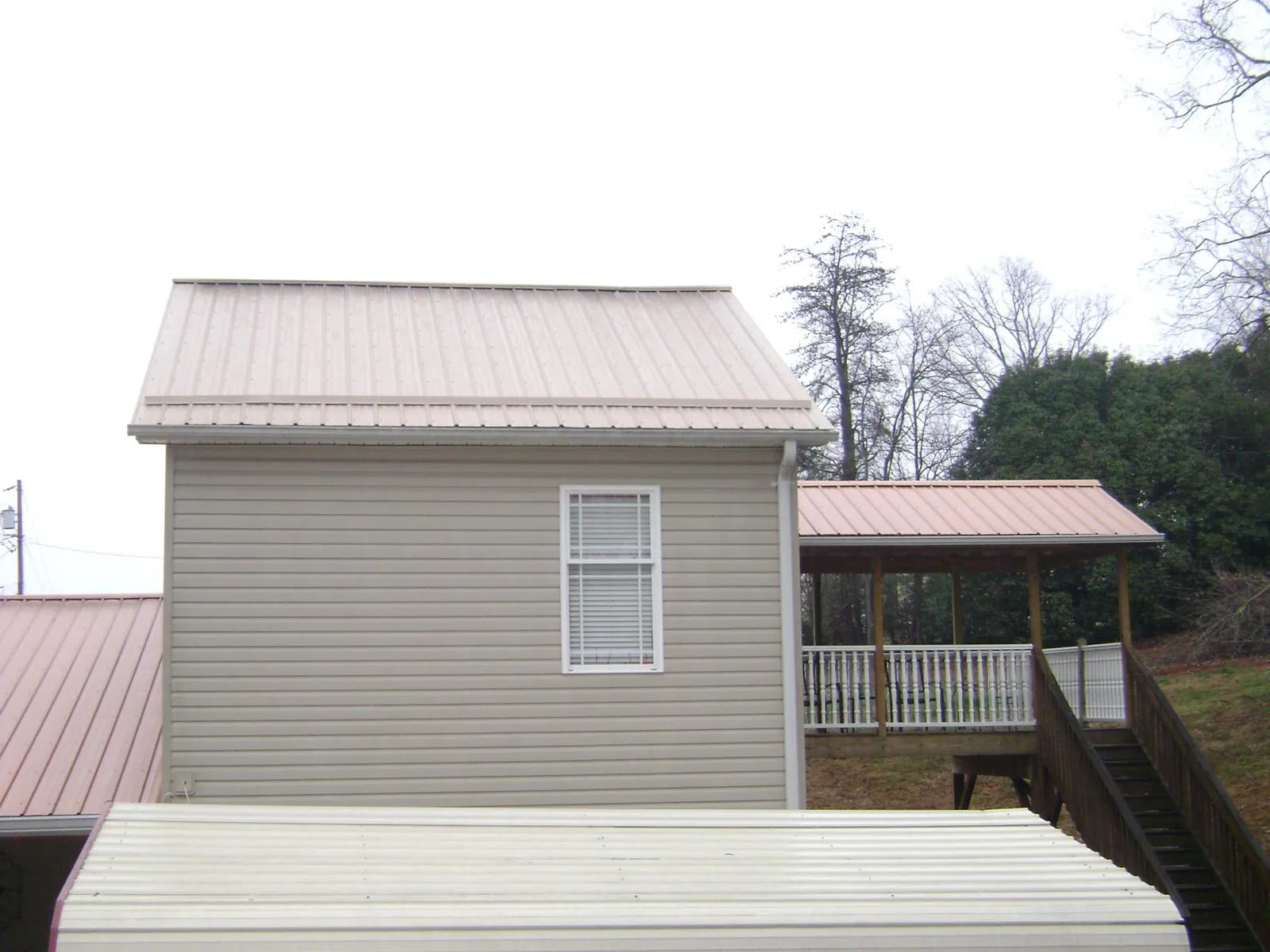 Tan metal roofs on a two story addition and attached porch, from a Roof Replacement job in Wellston